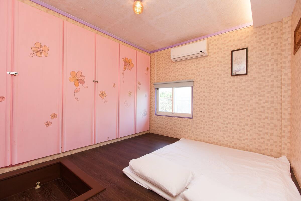 A bedroom with a bed, a window, a wardrobe with floral designs, and an air conditioning unit.