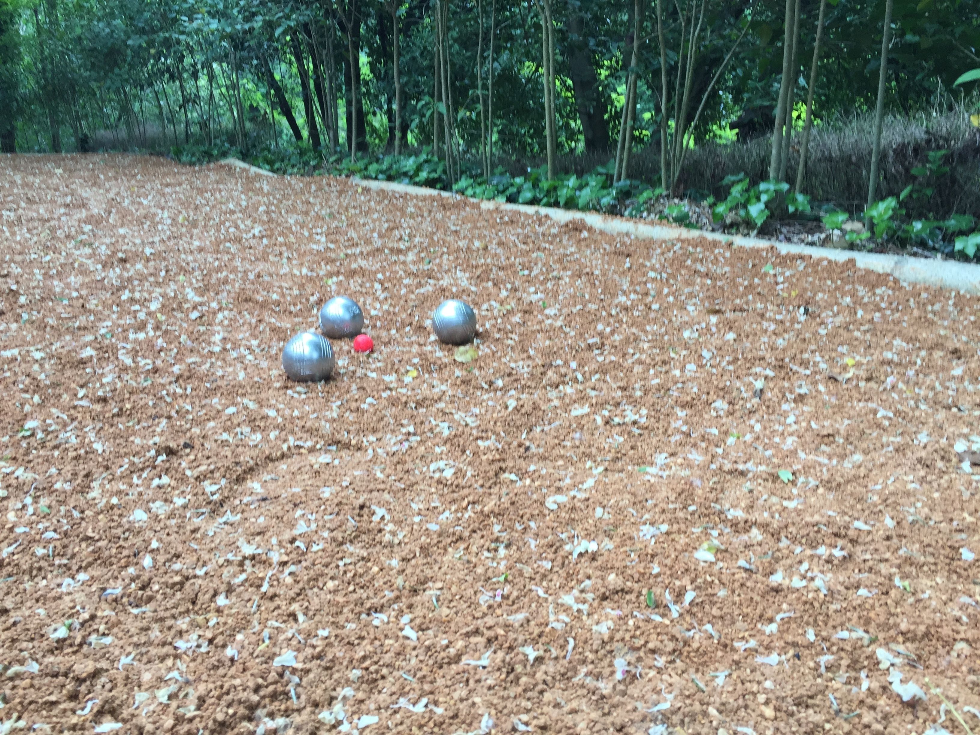 Un jardín con un sendero de tierra, esferas de metal y una pelota roja.