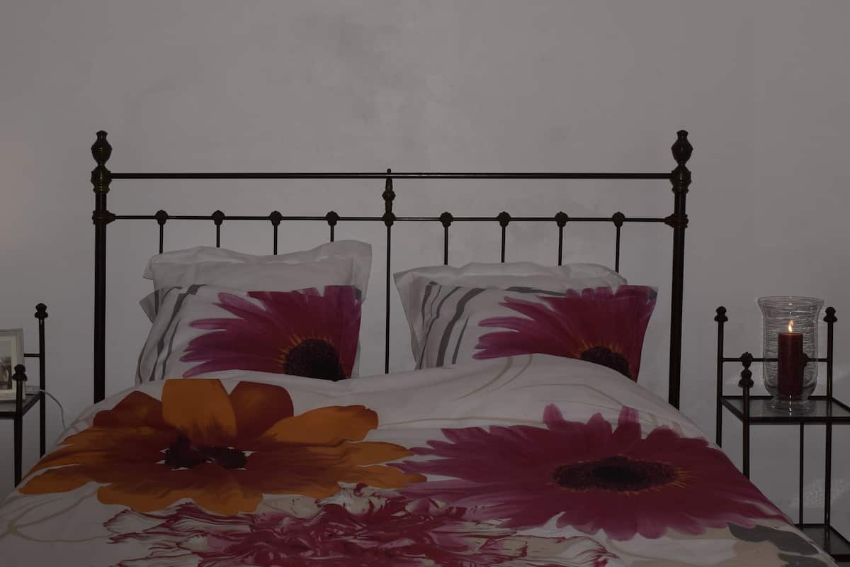 Un lit avec un cadre en métal, une table de chevet avec une lampe et un porte-bougie en verre.