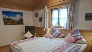 Un dormitorio con cama de madera, una silla, un ventanal con cortinas y decoración en la pared.