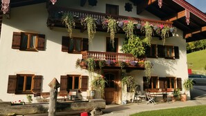 Un chalet tradicional con contraventanas de madera, un balcón con cestas de flores colgantes y mobiliario de exterior.