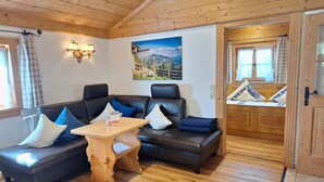 Una sala de estar acogedora con techo de madera, un sofá de cuero negro, una mesa de centro de madera y un cuadro con paisaje montañoso.