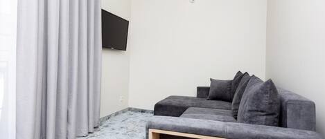 A modern living room with a grey sofa, a flat-screen TV mounted on the wall, and a light-colored floor.