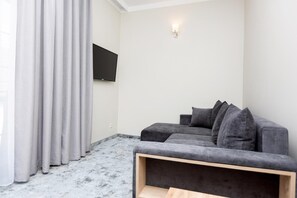 Una sala de estar moderna con un sofá gris, un televisor de pantalla plana montado en la pared y un piso de color claro.