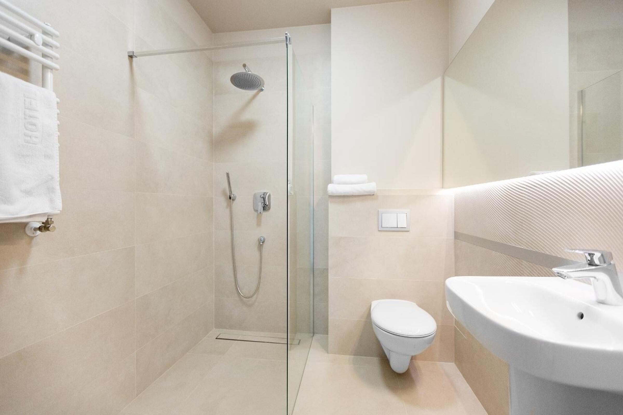 Un baño moderno con ducha envuelta en vidrio, inodoro blanco y lavamanos con espejo.