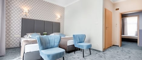 Une chambre d’hôtel avec un lit, deux chaises bleues, un mur à motifs et une porte donnant sur une autre pièce.