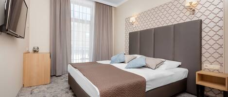 A hotel room with a large bed, a TV mounted on the wall, a bedside table, and a window with curtains.