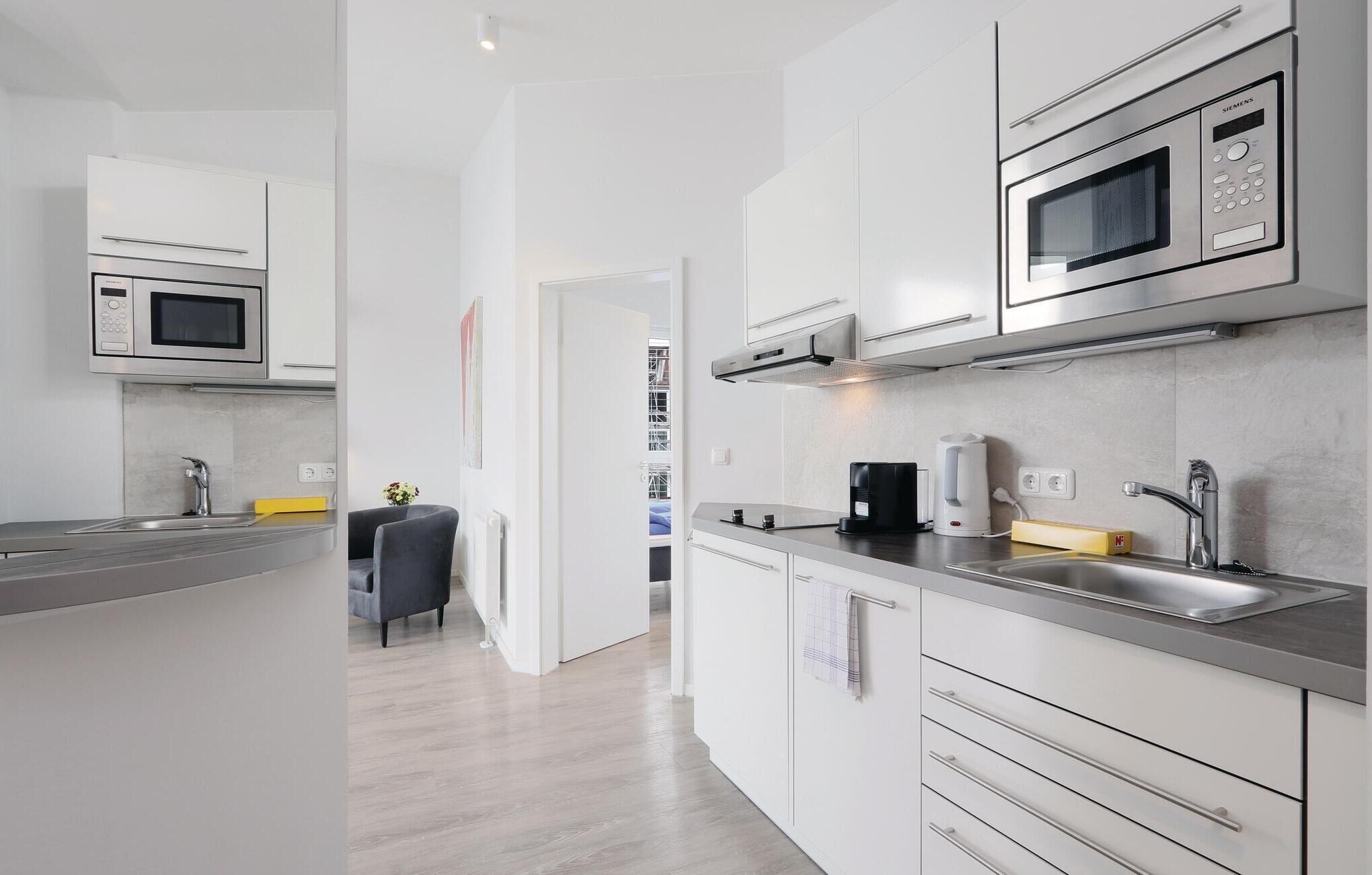Une cuisine moderne avec des meubles blancs, des appareils en acier inoxydable et un plan de travail gris.