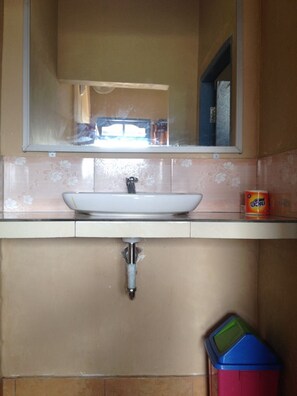 A bathroom with a white sink, a mirror above it, and a trash bin to the right. - Restu By View Hotel (Bayan)