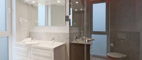 A modern bathroom with a glass shower enclosure, a double vanity with a large mirror, and a toilet.