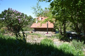 A rustic stone house with a red-tiled roof, surrounded by lush greenery and flowering trees. - Ca' de l'Ase B&B (Giusvalla)