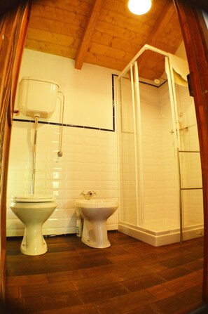 A bathroom with a wooden ceiling, white tiled walls, a shower enclosure, and two toilets. - Ca' de l'Ase B&B (Giusvalla)