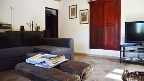 Una sala de estar con un sofá gris, una mesa de centro de madera con revistas, una puerta roja y un televisor sobre un mueble.