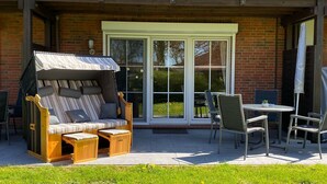 A patio with a wooden sofa, a covered table, and chairs. - Prigge vacation apartment (Brodersby)