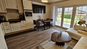 A compact kitchen with white cabinets, a dining table with chairs, and a sofa with a lamp. - Prigge vacation apartment (Brodersby)
