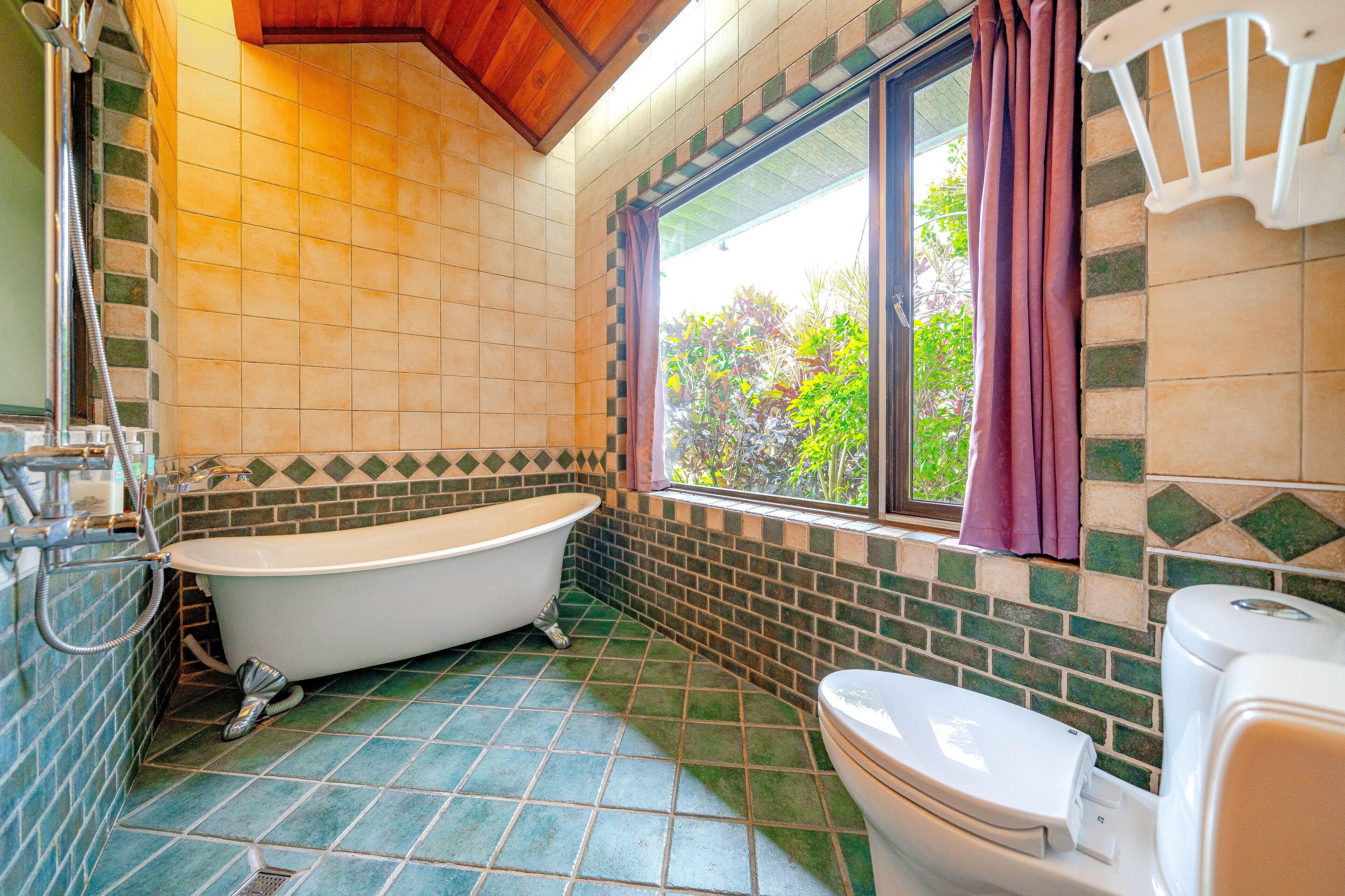 Et badeværelse med badekar, toilet og et vindue med gardiner.