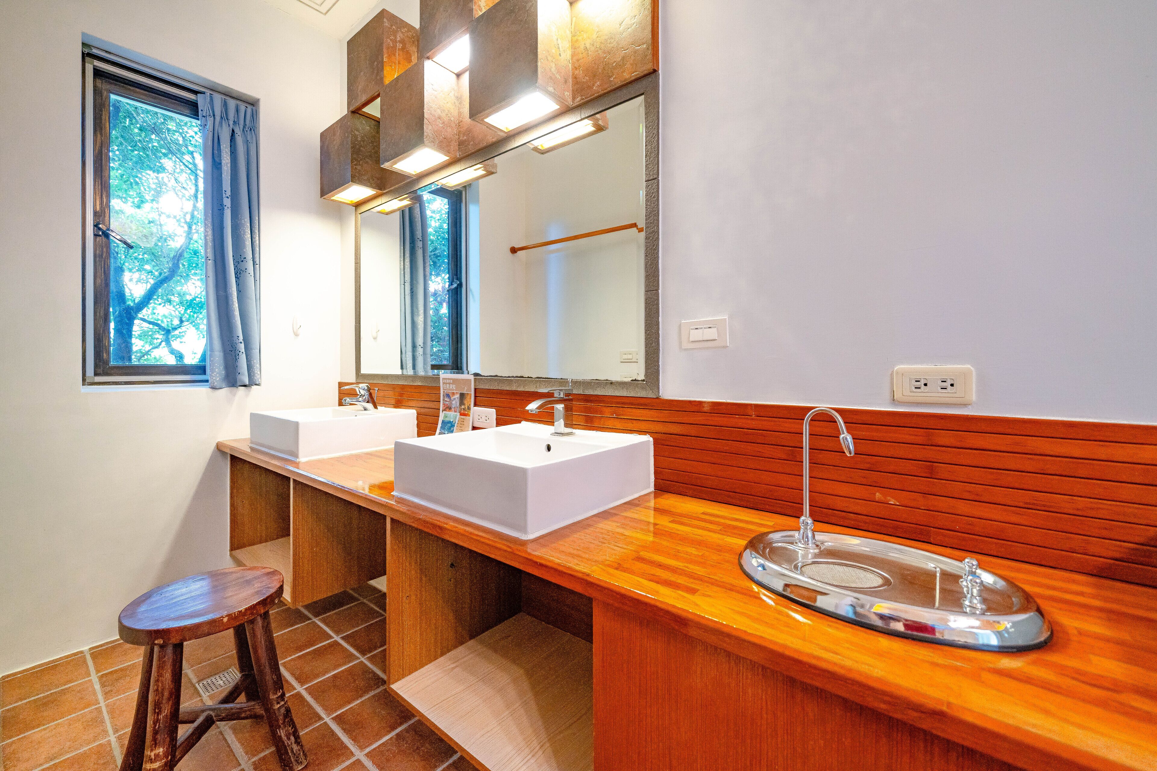 A modern bathroom with two sinks, a wooden vanity, a mirror, and a window with curtains.