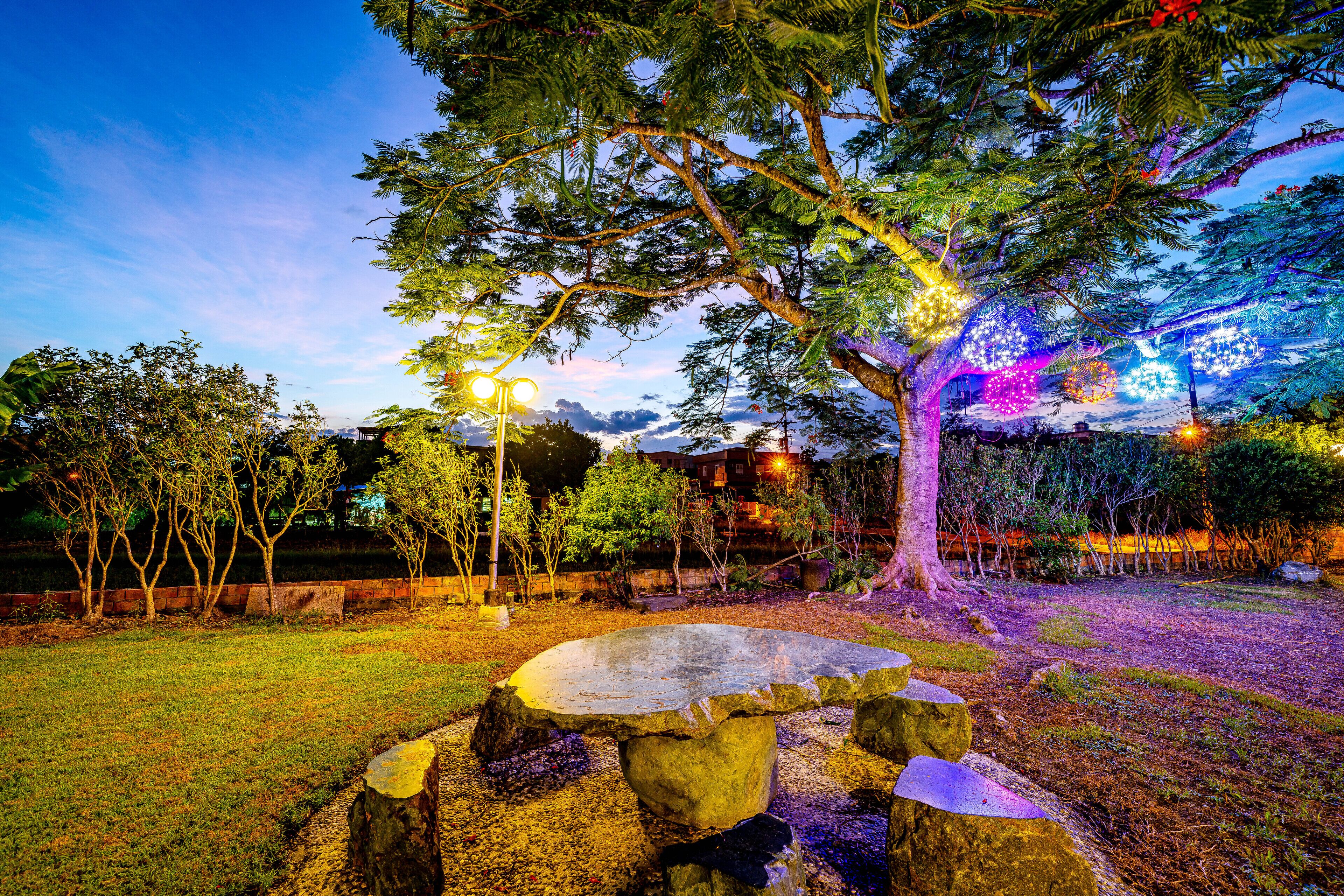 A stone bench surrounded by rocks, a tree with lights, and a grassy area.