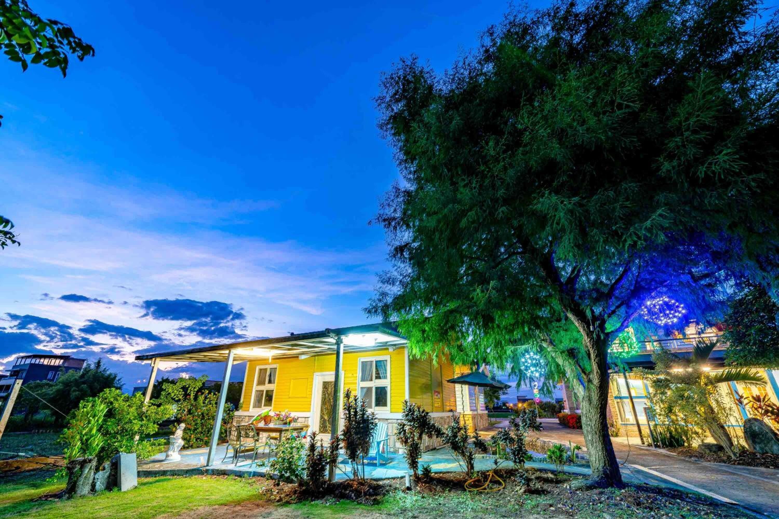 Una casa gialla con patio coperto e piscina, immersa nel verde e circondata da alberi.