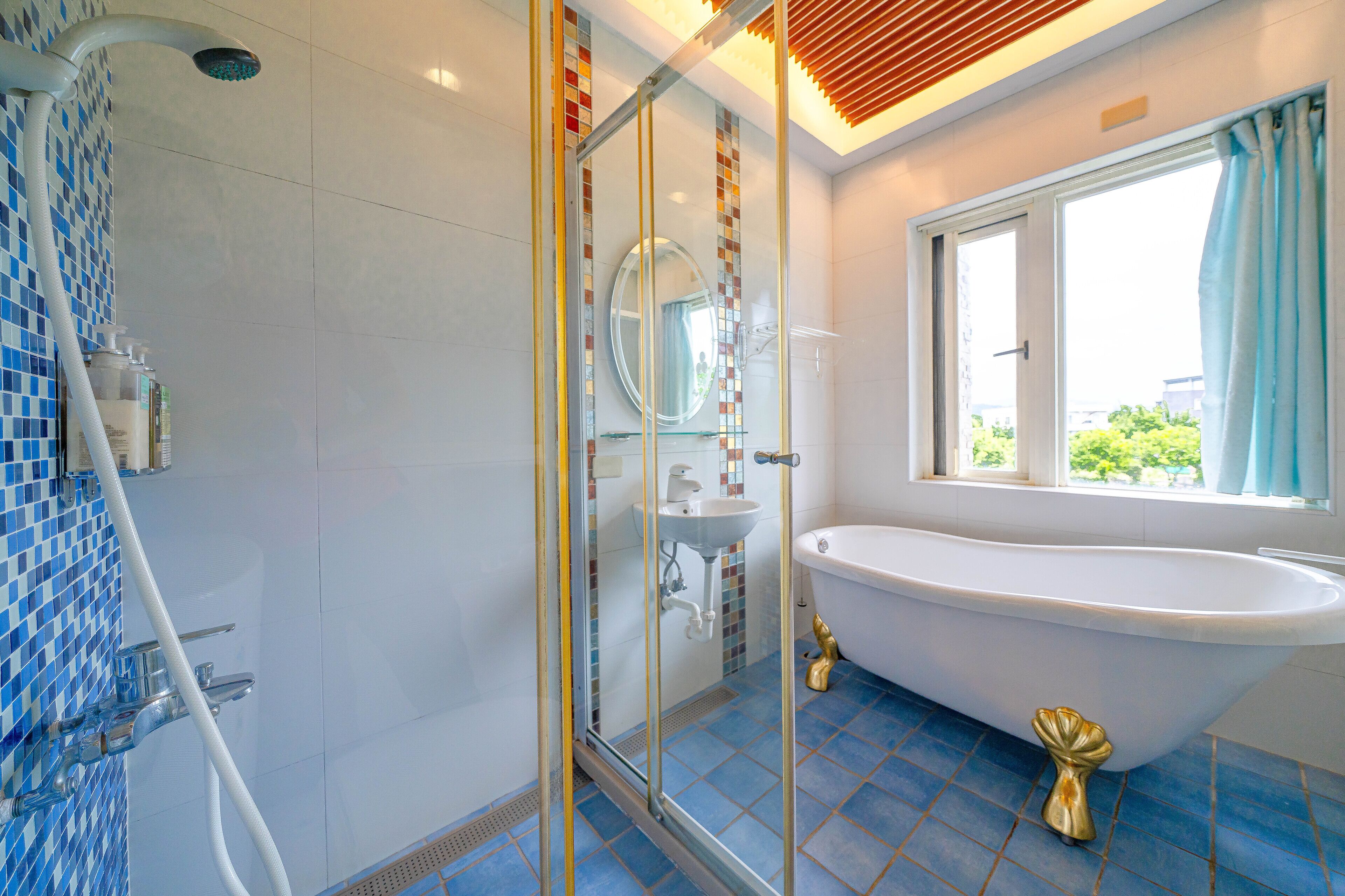 Une salle de bain dotée d’une douche à parois de verre, d’une baignoire sur pieds et d’une fenêtre avec des rideaux.
