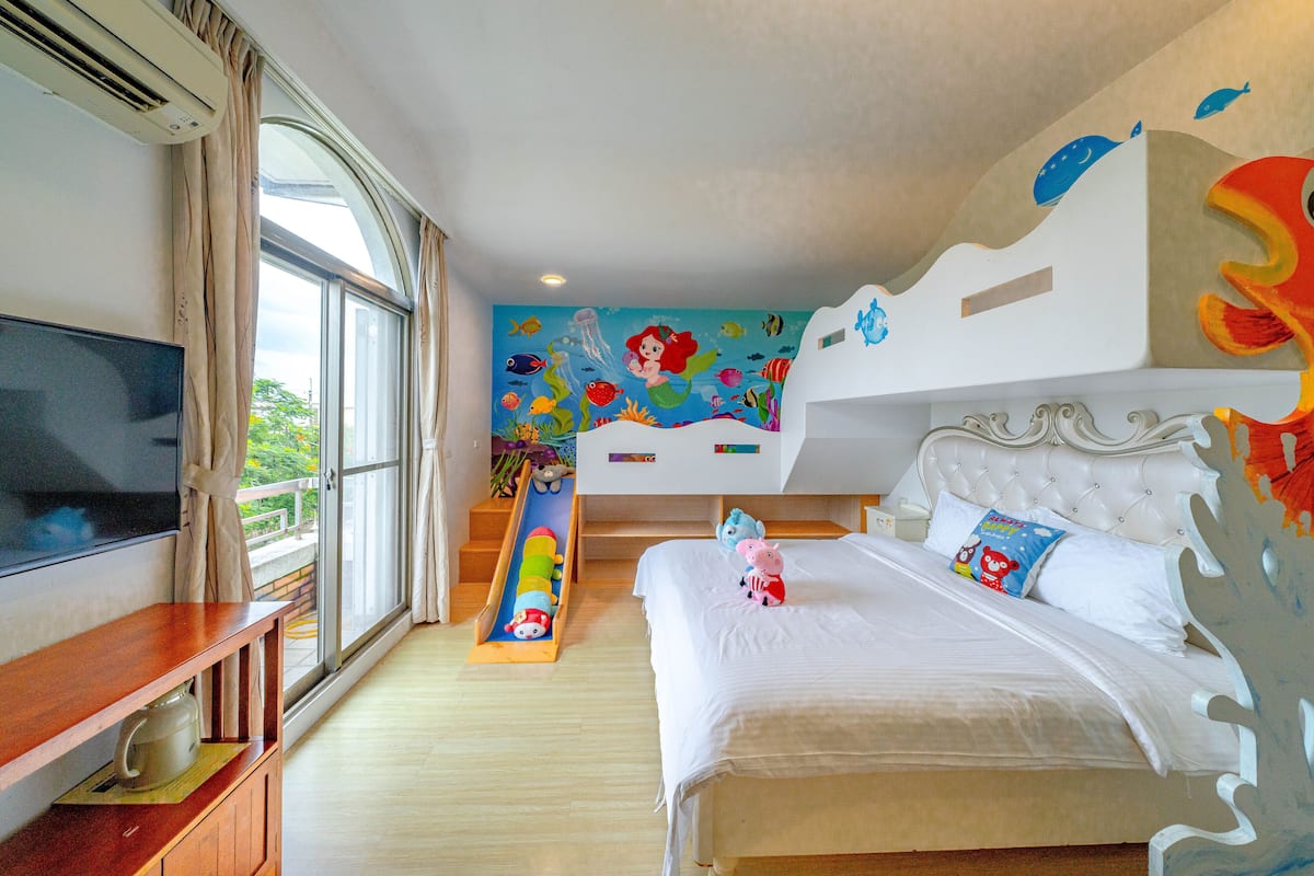 Un dormitorio con cama, televisión, ventana y un mural.