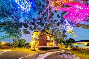A two-story house with a stone facade and a balcony, surrounded by trees and illuminated by string lights. - Rainbow Garden B&B (Dongshan)