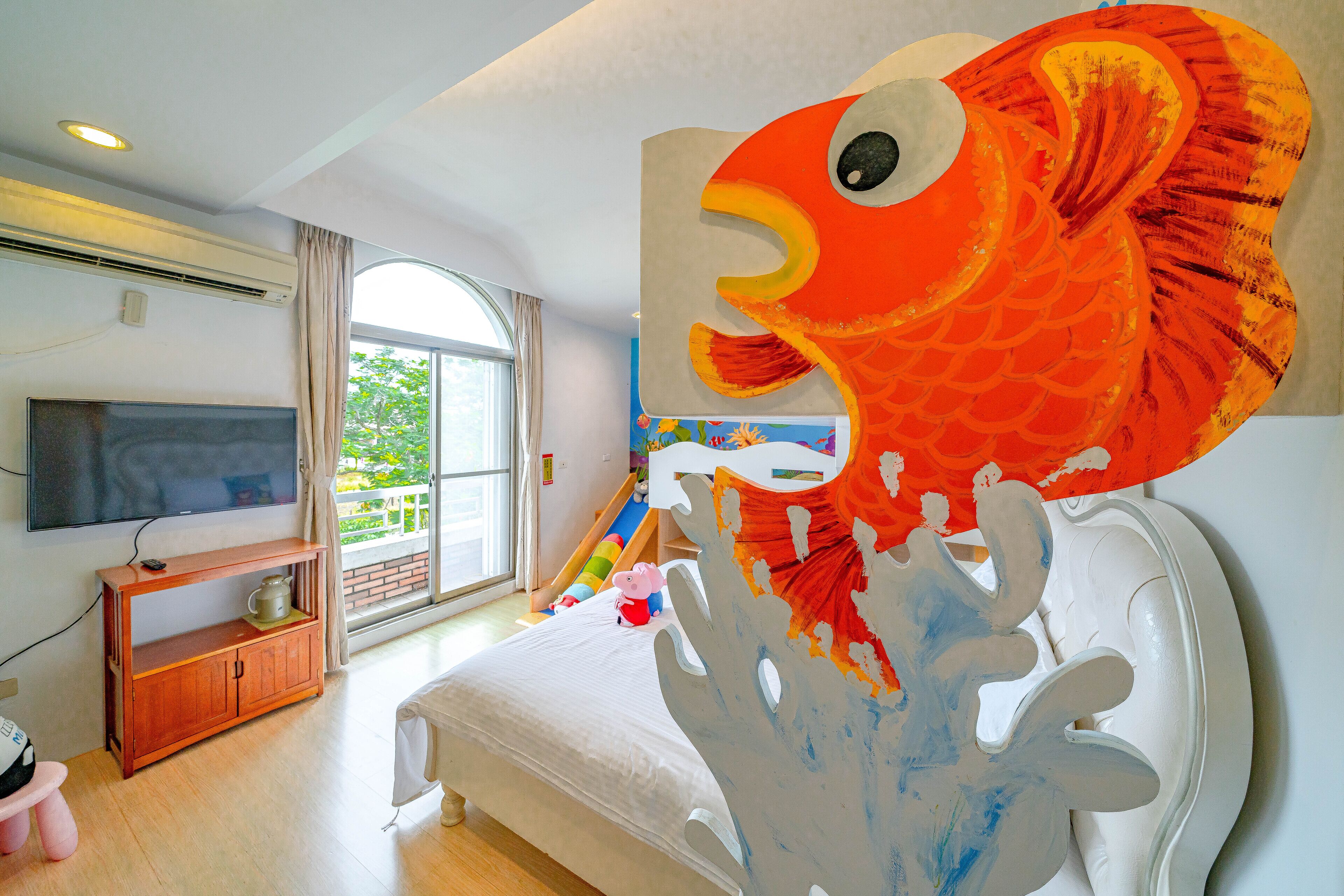 Un dormitorio con cama, televisor, aparador de madera y un cuadro grande con peces en la pared.
