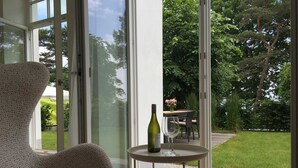 A modern room with a large sliding glass door leading to a garden. There is a round table with a bottle and a glass, and a patterned chair. - Holiday apartment 01 Villa Seeblick on the beach of Binz - Villa Seeblick Binz (Binz)