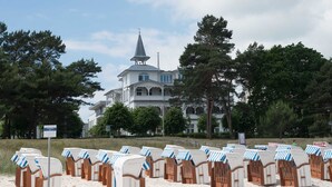 A beach with rows of beach chairs and a large building with a steeple in the background. - Holiday apartment 01 Villa Seeblick on the beach of Binz - Villa Seeblick Binz (Binz)