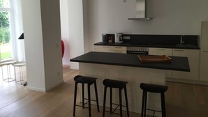 A modern kitchen with a black countertop, stainless steel appliances, and three bar stools. - Holiday apartment 01 Villa Seeblick on the beach of Binz - Villa Seeblick Binz (Binz)