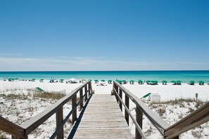 Een houten looppad leidt naar een strand met groene parasols.
