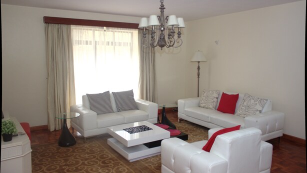 A living room with two white sofas, a glass coffee table, a chandelier, and a floor lamp. - Brooks (Nairobi)