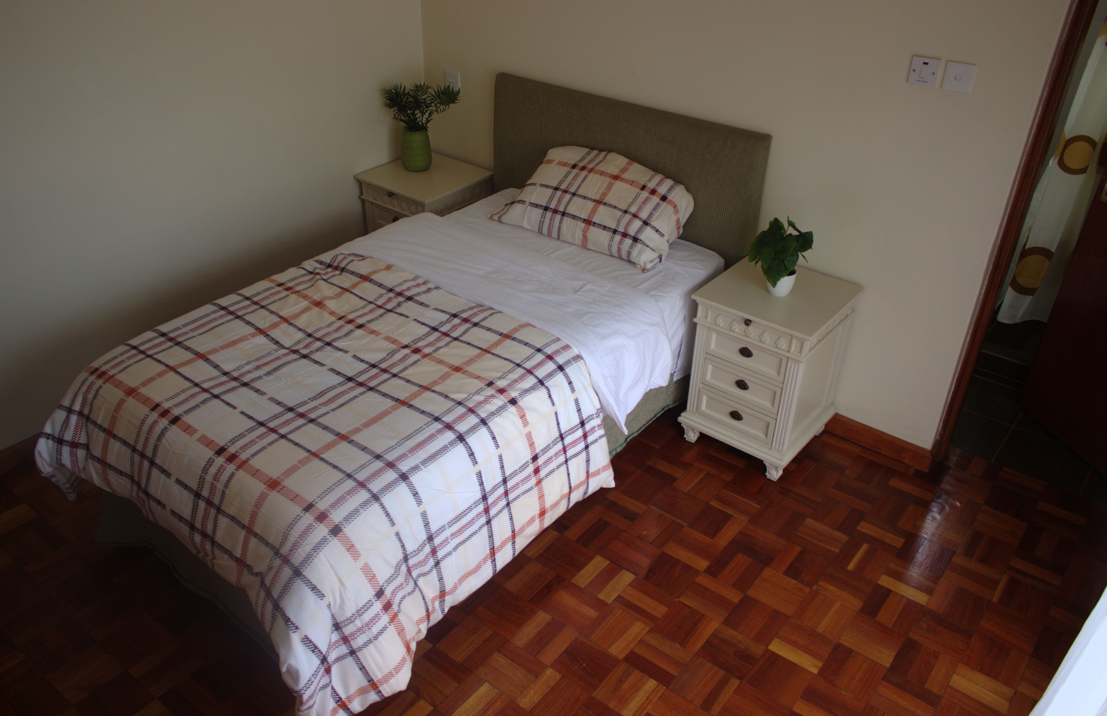 A bedroom with a bed, a nightstand, a dresser, and a potted plant.