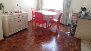 A dining area with a round table and red chairs, a white cabinet, and a kitchen area with a coffee machine. - Brooks (Nairobi)