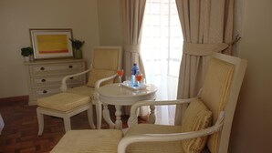 A room with a dining table, two chairs, a small cabinet, and a window with curtains. - Brooks (Nairobi)