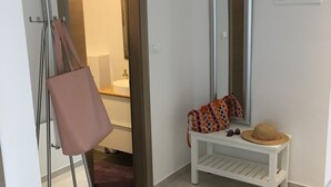 Een kamer met een witte bank, een spiegel, een deur naar een andere kamer en een kapstok met een tas.