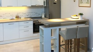 Een moderne keuken met witte kasten, een roestvrijstalen koelkast en een bar met twee krukken.