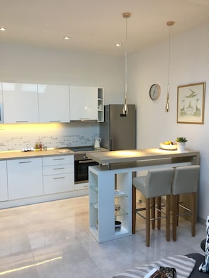 A modern kitchen with white cabinets, a stainless steel refrigerator, and a bar area with two stools.