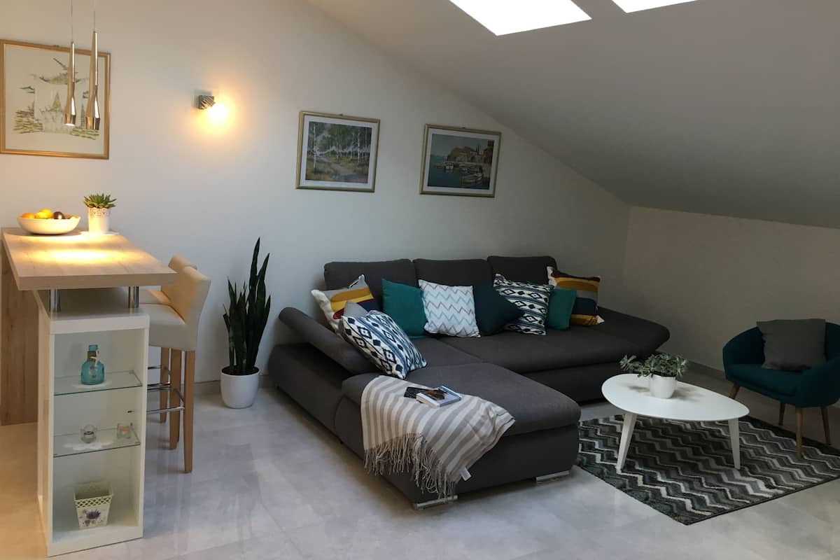 A modern loft apartment with a large gray sofa, a small round table, and a skylight.
