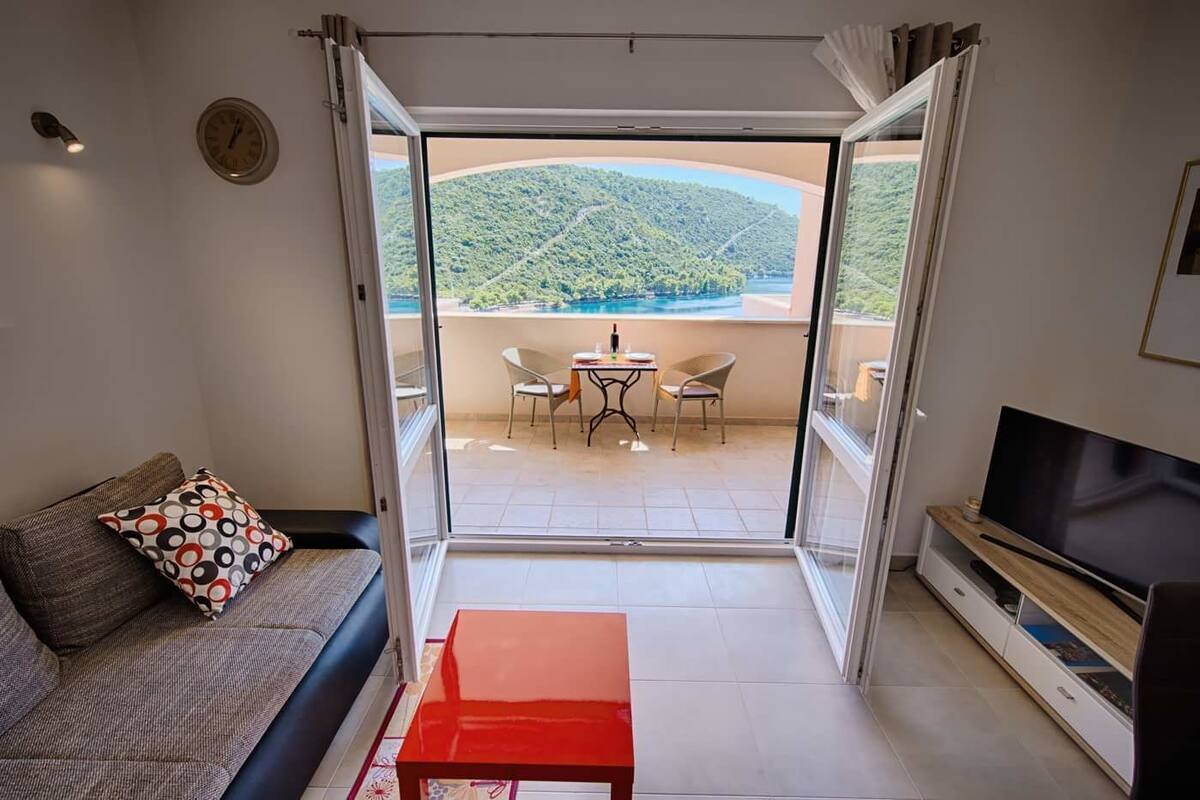 A modern living room with a sofa, a red table, a TV, and a balcony with a table and chairs.