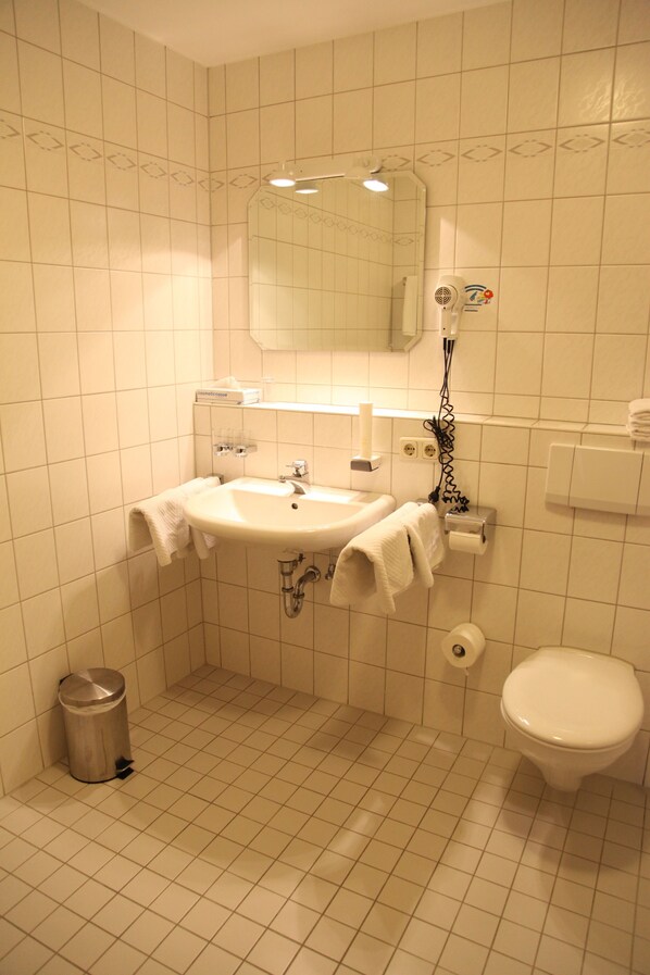 A bathroom with a sink, mirror, toilet, and a trash can.