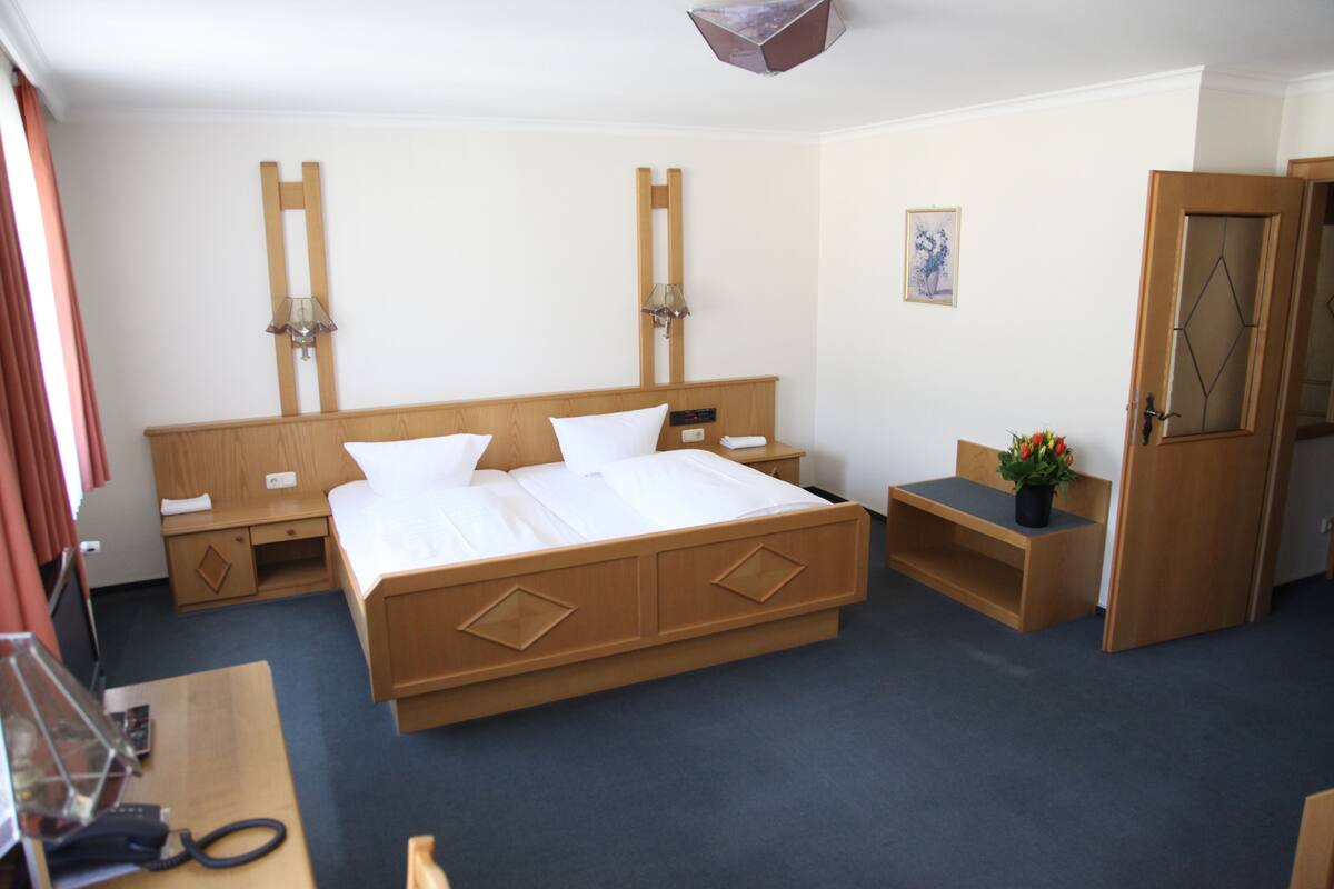 Una habitación de hotel con una cama grande, mesitas de noche, un escritorio, un armario y una pequeña planta en maceta.