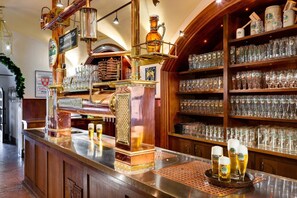 Una zona de bar con un grifo de cerveza de cobre, estantes llenos de vasos de cerveza y una barra de madera.