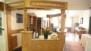 A reception area with a wooden reception desk, a potted plant with red flowers, and a bookshelf. - Brauereigasthof Buergerbraeu (Bad Reichenhall)