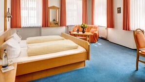 A hotel room with a bed, a small table with a vase, a chair, and a window with curtains. - Brauereigasthof Buergerbraeu (Bad Reichenhall)