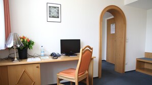 A hotel room with a wooden desk, a chair, a computer, a lamp, a plant, and a door. - Brauereigasthof Buergerbraeu (Bad Reichenhall)
