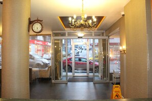 Entrada d'hotel amb una porta giratòria, un rellotge i una làmpada penjolant.