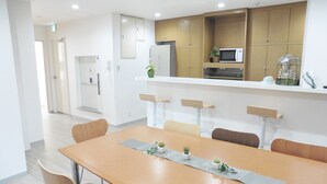 Un espace repas moderne avec une longue table en bois, plusieurs chaises et un coin cuisine doté de meubles en bois et d’un four à micro-ondes.