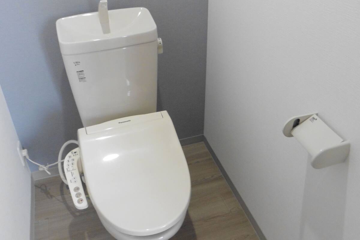 Une petite salle de bain moderne équipée de toilettes, d’un porte-rouleau de papier toilette et d’une prise électrique visible.