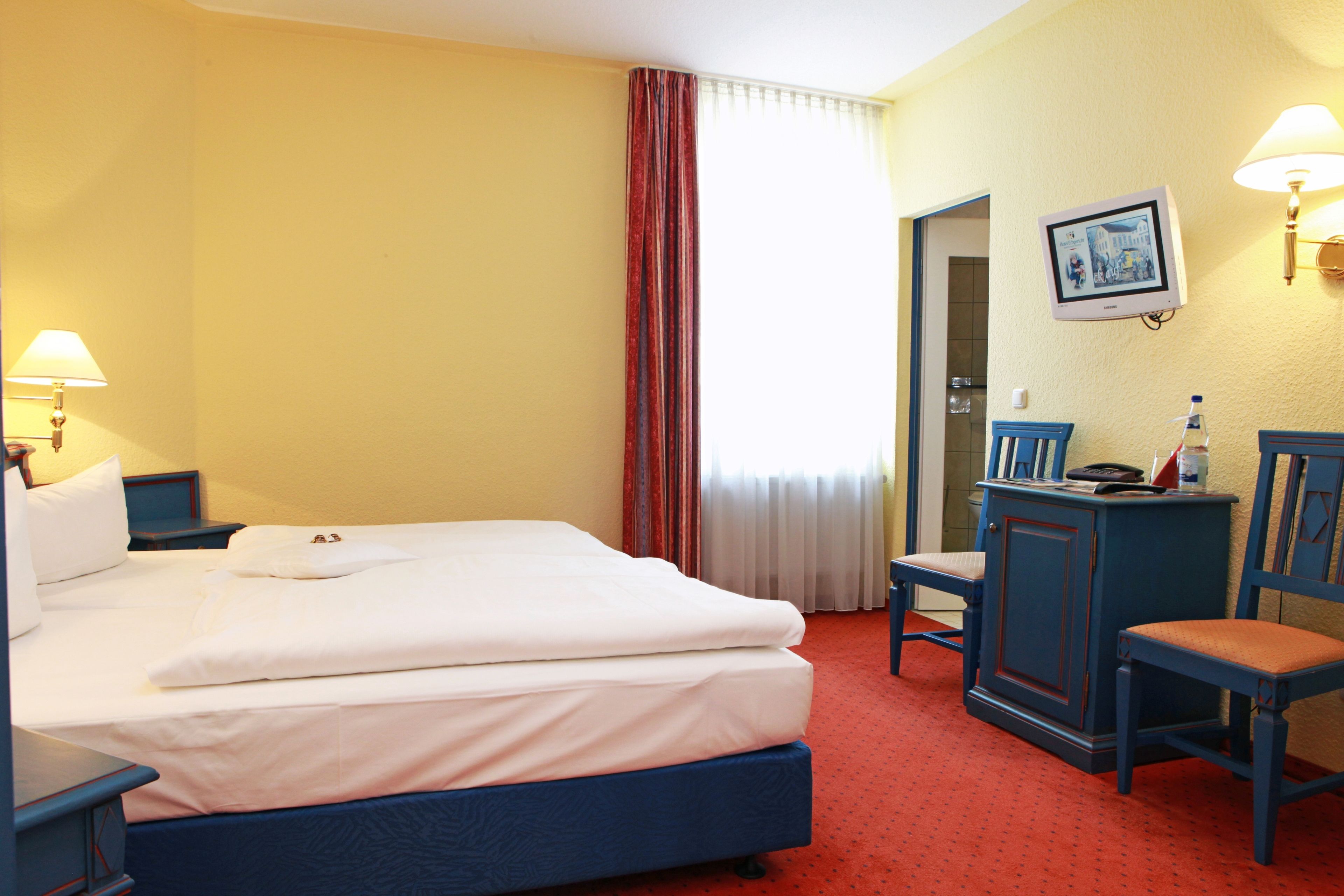 A hotel room with a bed, a desk, a chair, a lamp, and a picture on the wall.